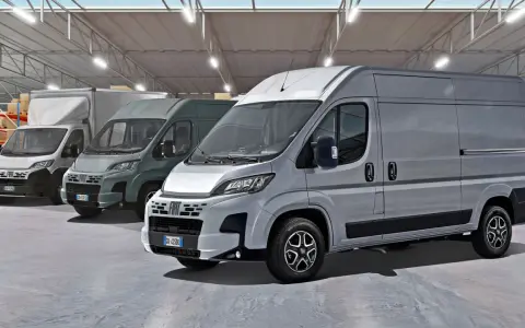 Rząd szarych furgonetek Fiat Ducato Maxi w magazynie z półkami i pudełkami.
