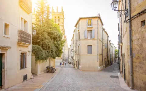 Ruelles pavées et bâtiments ocres, un aperçu des meilleurs quartiers de Montpellier. Des vélos attendent, des passants flânent sous le soleil.