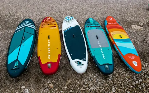 Pięć kolorowych desek z wiosłem leży na plaży. Gotowe na przygodę na wodzie!