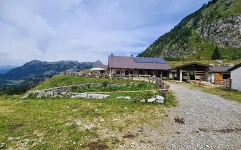 Malga Tuglia, un rifugio alpino con pannelli solari, immerso nel verde con montagne sullo sfondo.