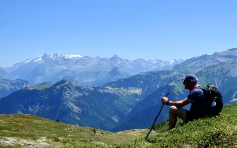 Un randonneur léger profite d'une vue panoramique sur les montagnes. Il est assis sur une colline verdoyante, bâton à la main, admirant le paysage majestueux.