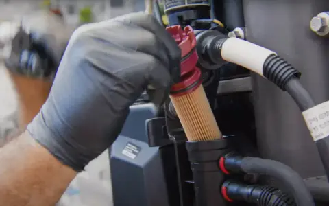 Main d'un mécanicien en gant noir retirant un filtre à gasoil encrassé, conséquence d'un mauvais entretien.