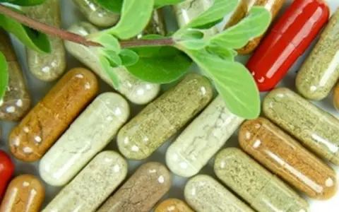Cápsulas de suplementos naturales de varios colores y hojas verdes.