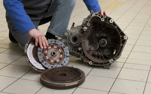 Mechanik prezentuje części po demontażu skrzyni biegów, przygotowując się do wymiany łożyska oporowego.