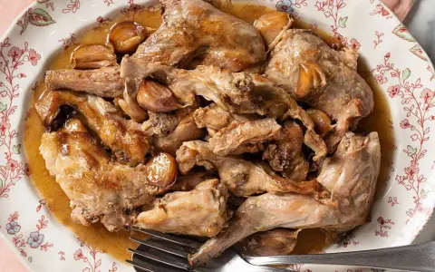 Conejo al ajillo servido en un plato con borde floral, con trozos de carne dorada y dientes de ajo enteros.