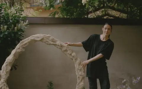 Kajsa Melchior står vid en skulptur i en trädgård.