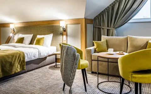 Przytulny pokój hotelowy z dwoma łóżkami, kanapą i fotelami. Idealne miejsce na relaks po podróży.