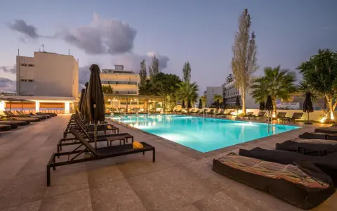 Basen hotelowy oświetlony nocą, leżaki i palmy. Idealne miejsce na relaks, zgodnie z licznymi heronissos hotel opinie.