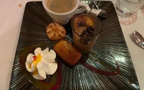 Un assortiment gourmand : café, financier, macaron, verrine chocolat et chantilly, servi sur une assiette noire texturée, digne de la taverne des fougères.