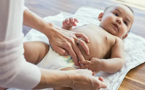 Rąk opiekuna zmienia pieluszkę niemowlęciu. Czy to powód, dlaczego 2 miesięczne dziecko nie sika w nocy?