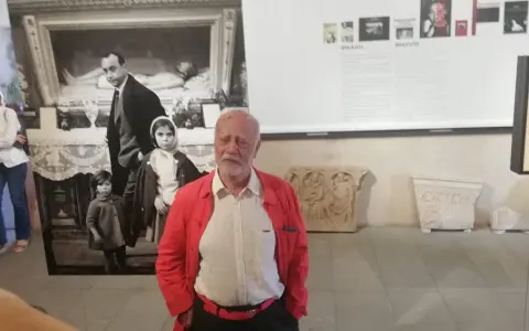 Un uomo anziano con giacca rossa, davanti a una foto di Ferdinando Scianna in Sicilia con bambini.