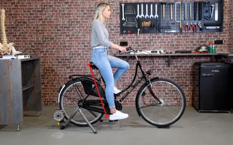 Frau sitzt auf einem Fahrrad auf einem Rollentrainer. Ein roter Pfeil zeigt die richtige Höhe des Fahrradsattels an, um den Fahrradsattel richtig einzustellen.