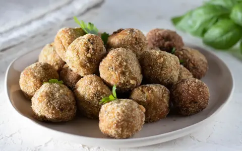 Un piatto pieno di polpette di melanzane dorate e croccanti, guarnite con prezzemolo fresco.