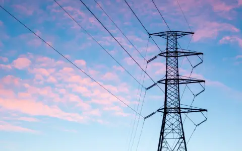 Wieża z przewodami linii energetycznej średniego napięcia na tle różowo-niebieskiego nieba.