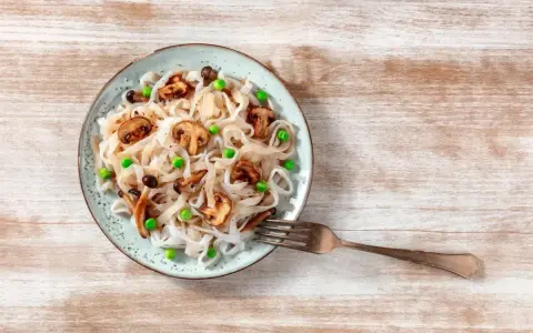 Makaron konjac jak smakuje? Delikatny, z grzybami i groszkiem, na talerzu.