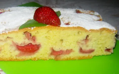Wilgotne ciasto na oleju z owocami, posypane cukrem pudrem, z truskawką na wierzchu.