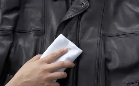 Delikatne czyszczenie kurtki skórzanej białą ściereczką. Skóra jest czarna, z widocznymi szwami.