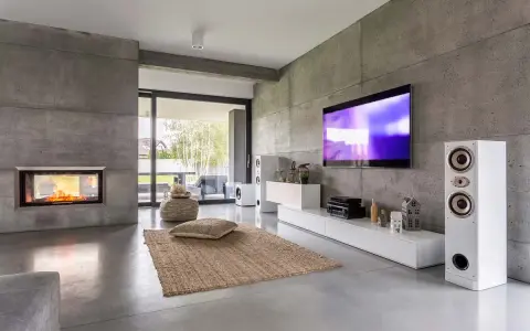 Nowoczesny salon z betonowymi ścianami w stylu brutalizm, kominkiem, telewizorem i głośnikami.