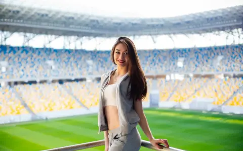 Uśmiechnięta dziewczyna w sportowym stroju na tle stadionu. Idealny pomysł, jak się ubrać na mecz, by czuć się komfortowo i stylowo.