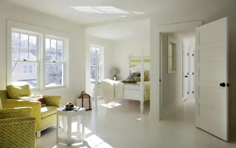 Luminosa camera da letto con **colore pareti bianco caldo**, due poltrone gialle, letto a baldacchino e luce solare che filtra dalle finestre.