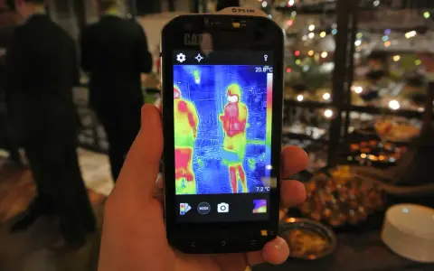 Ręka trzyma smartfon Cat S60 z włączoną termowizją, pokazującą dwie osoby w cieplejszych barwach.