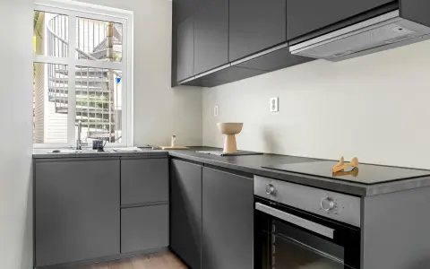 Diseño cocina restaurante moderno con gabinetes grises, encimera oscura y ventana con escalera exterior.