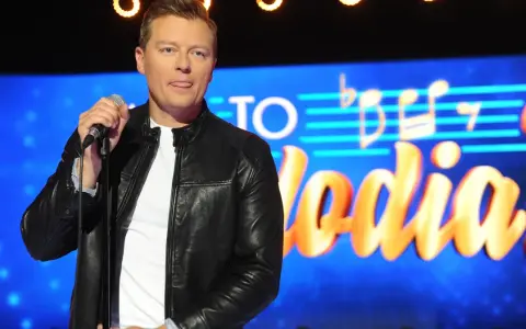 Rafał Brzozowski z mikrofonem na scenie, w tle napis "Jaka to melodia?".
