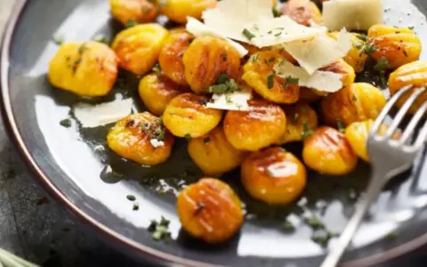 Gnocchis dorés à la sauce butternut, parsemés de copeaux de parmesan et d'herbes fraîches. Un délice réconfortant.
