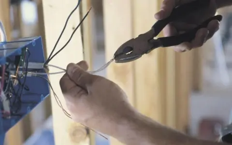 Ręce przycinają przewody do skrzynki elektrycznej. To kluczowy krok, by dowiedzieć się, jak zostać elektrykiem.
