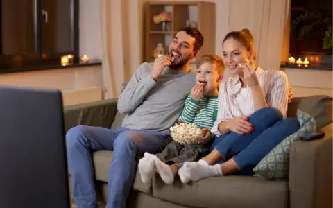 Rodzina zajada popcorn podczas oglądania filmów familijnych.