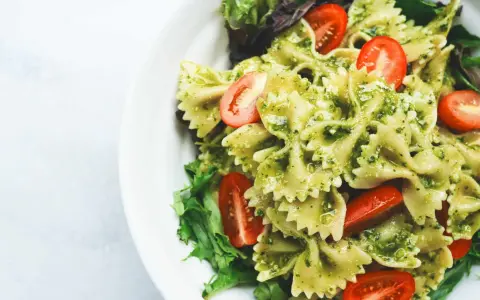 Ein köstlicher Nudelsalat mit Pesto, garniert mit frischen Kirschtomaten und Salatblättern.