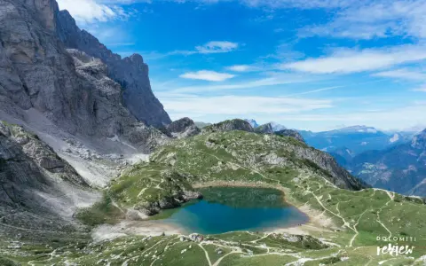Lago di Coldai, incastonato tra le maestose vette delle Dolomiti, con sentieri che si snodano sui prati verdi.