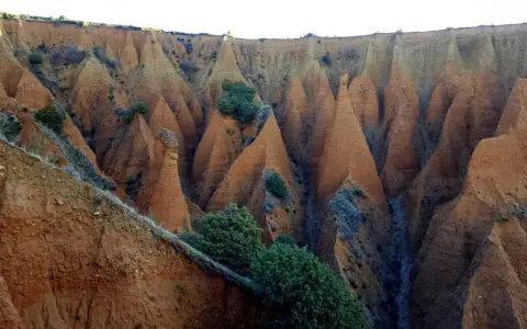 Paisaje erosionado con formaciones cónicas de tierra rojiza, vegetación escasa y un camino que parece el pontón de la oliva ruta circular.