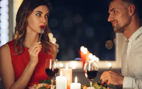 Romantyczna kolacja przy świecach. Ona, w czerwonej sukience, zmysłowo je, a on patrzy na nią z uwielbieniem. Widać oznaki flirtu dziewczyny w jej spojrzeniu.