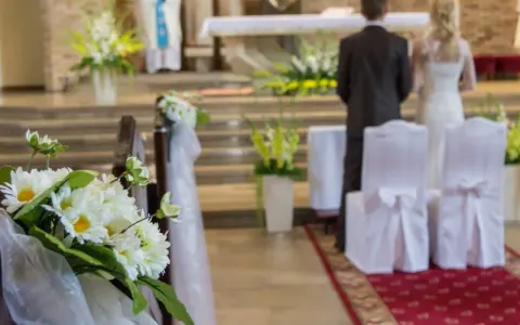 Kwiaty zdobią kościelną nawę. Para młoda stoi przy ołtarzu, przygotowując się do ślubu kościelnego jednostronnego.