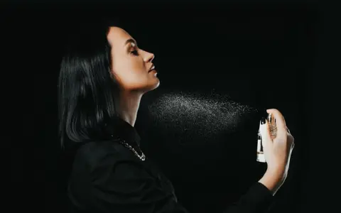 Kobieta rozpyla perfumy na szyję na czarnym tle.