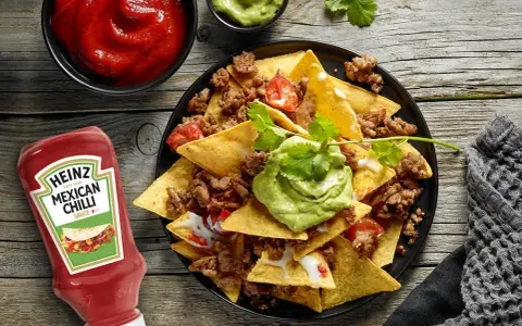 Nachos con carne, guacamole y salsa en un plato negro, con botella de Heinz y cuencos de salsa.