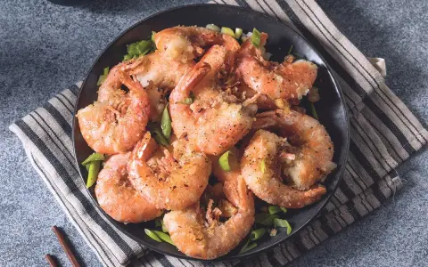 Gamberi sale e pepe croccanti, serviti su un piatto scuro con erba cipollina fresca. Un piatto invitante e saporito.