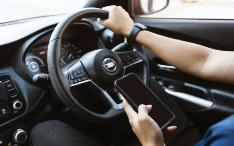 Fahrer hält Handy in der Hand, während er fährt. Hoffentlich wird er nicht geblitzt mit Handy in der Hand!