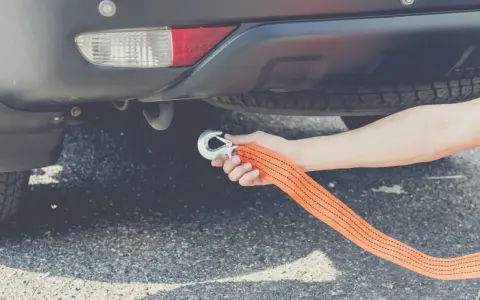 Dłoń mocuje hak liny holowniczej do haka holowniczego auta. To pokazuje, czy można holować auto na linie.