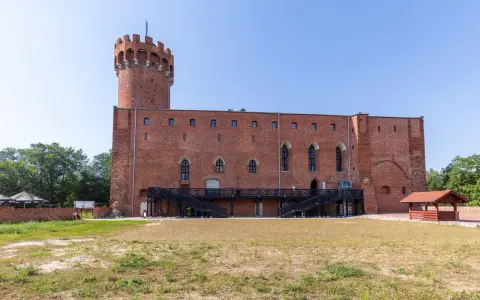 Zamek w Świeciu, ceglana twierdza z wieżą, otoczona zielenią i dziedzińcem.