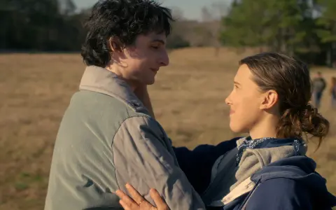 Mike i Eleven z Stranger Things 002 patrzą na siebie z czułością na tle polnej scenerii.