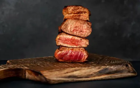 Gestapelte, saftige Steak-Scheiben, perfekt englisch gebraten, auf einem rustikalen Holzbrett.