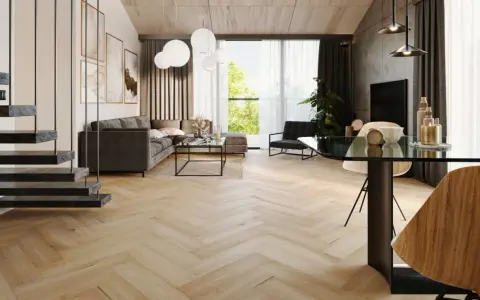 Nowoczesny salon z szarą sofą, szklanym stolikiem i jadalnią. Wzrok przyciągają panele bez dylatacji w progu, tworzące jednolitą, drewnianą podłogę w jodełkę.