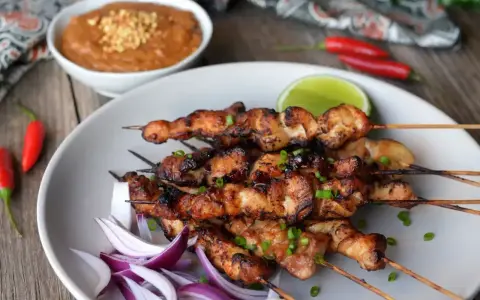 Pyszne satay z kurczaka na patyczkach, podane z sosem orzechowym, limonką i papryczkami chili.