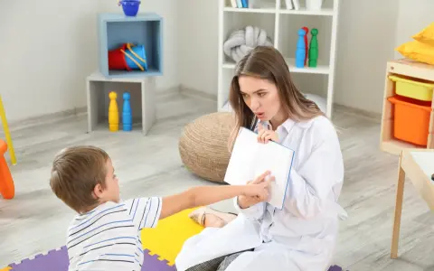 Terapeuta pracuje z dzieckiem nad poprawą niewyraźnej mowy, wskazując palcem na strony otwartej książki.