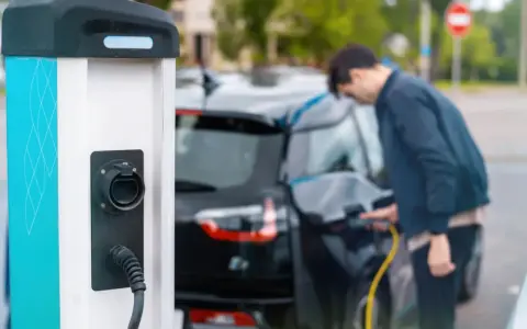 Mój elektryk czeka na ładowanie. Mężczyzna podłącza kabel do samochodu przy stacji ładowania.