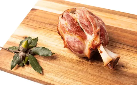 Codillo de cerdo asado, jugoso y dorado, reposa sobre una tabla de madera junto a unas bellotas.