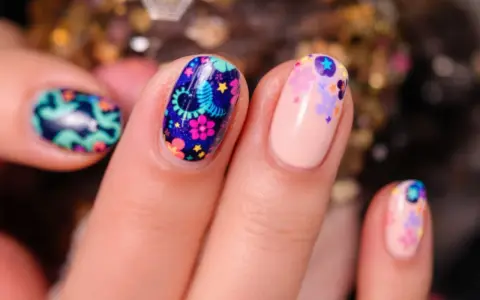Comment avoir de beaux ongles : des ongles décorés de motifs floraux colorés et de petites étoiles sur fond bleu nuit ou nude.