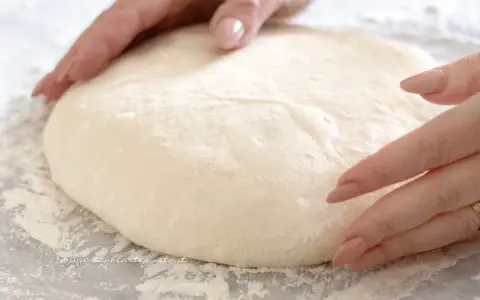Mani che lavorano un impasto pizza veloce, soffice e pronto per essere steso.